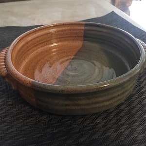 May include: A brown and green ceramic baking dish with two handles. The dish is glazed and has a speckled finish.