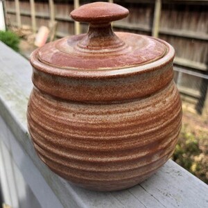May include: A brown and white ceramic jar with a lid. The jar has a rounded shape and is decorated with horizontal stripes.