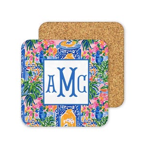 a square coaster with a vibrant floral pattern and a monogrammed logo.