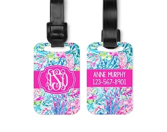 May include: Two rectangular luggage tags with black leather straps. The tags feature a vibrant floral pattern in shades of blue, pink, and green. One tag displays a white monogram with the letters LSD, while the other shows the text ANNE MURPHY 123-567-8901.