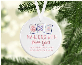 Könnte beinhalten: Ein rundes, weißes Keramikornament, das an einem weißen Band hängt. Das Design zeigt drei Mahjong-Spielsteine, den Text "MAHJONG WITH Mah Girls" in Pink und eine Liste von Namen: JULIA, DANIELLE, ISLA, JENNIE, KATIE, GRACE, BETH & LAURA.