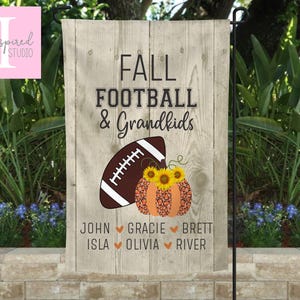 May include: A rectangular garden flag with a light wood grain background featuring the text FALL FOOTBALL & GRANDKIDS. Below the text is a brown football next to an orange leopard print pumpkin topped with three yellow sunflowers. Six names are listed at the bottom separated by small orange hearts.