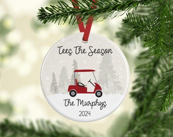 Può includere: Addobbo natalizio rotondo bianco con un golf cart rosso, alberi innevati e il testo "Tees The Season The Murphys 2024".