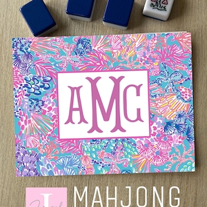 May include: A colorful Mahjong card sticker with a floral pattern in shades of pink, blue, and purple. The sticker features a white rectangle with the letters "AMC" in pink. Four Mahjong tiles are placed above the sticker.