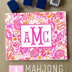 May include: A rectangular sticker featuring a vibrant pattern of pink and orange seashells, starfish, and flowers on a light background. A central white rectangle contains the hot pink monogram letters AMG. Four mahjong tiles are placed above.
