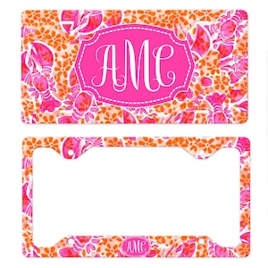 May include: A pink and orange license plate frame with a lobster design and the monogram "AMC" in a pink oval.