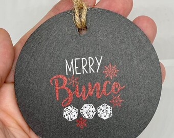 May include: A black round slate ornament with a white and red design that says "Merry Bunco" with three white dice and snowflakes.