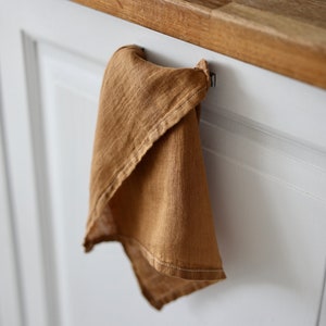 May include: A brown linen kitchen towel hanging on a hook on a white cabinet door.