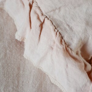 May include: Close-up of a pale pink fabric with a ruffled edge. The fabric has a soft, textured appearance.