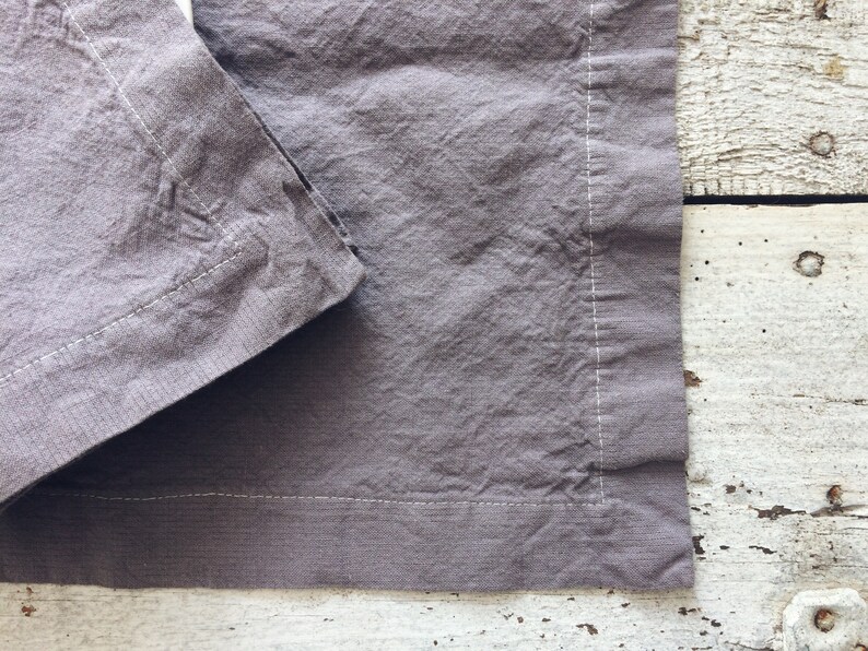 May include: A gray linen napkin with a white stitched border. The napkin is folded in half and the edges are visible.