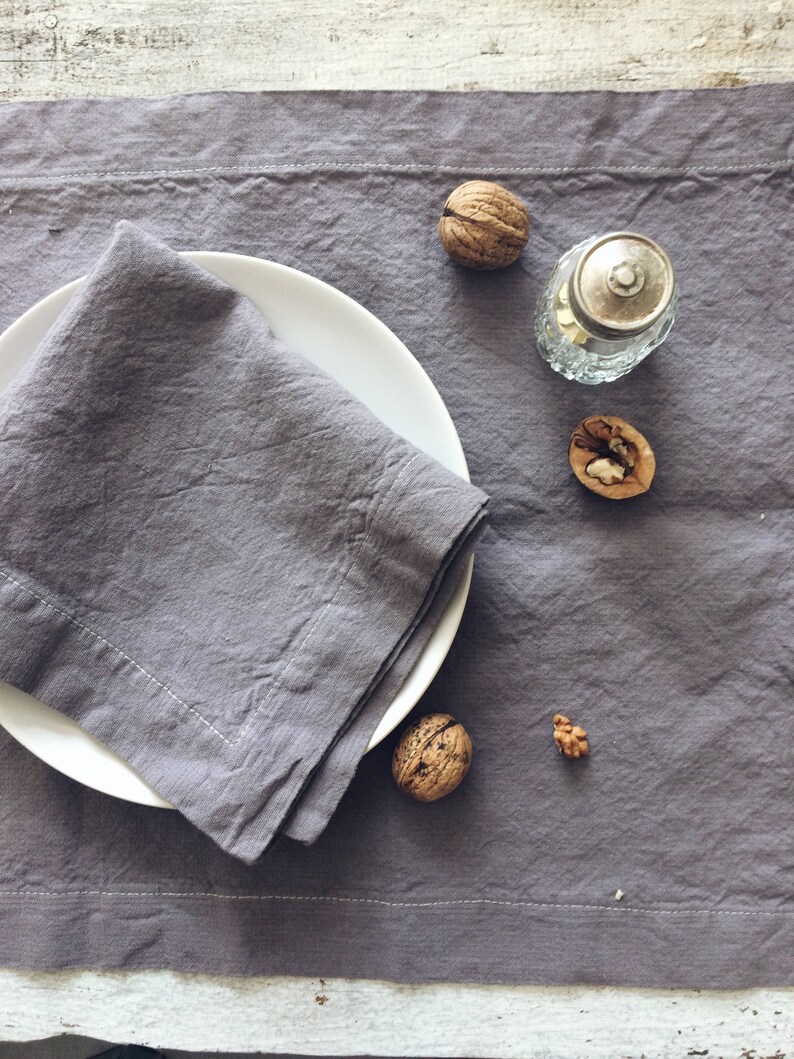 May include: A gray linen napkin folded on a white plate, with walnuts and a glass salt shaker on a gray linen tablecloth.