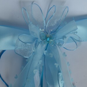 Puede incluir: Una cinta de sat&eacute;n azul claro con un lazo azul transparente y un adorno de mariposa plateada. El lazo est&aacute; decorado con peque&ntilde;os corazones azules.