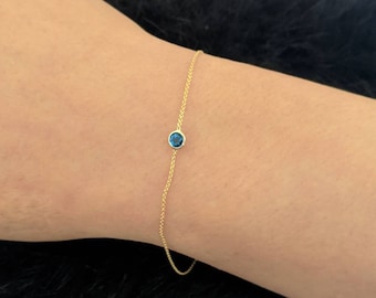 May include: A delicate gold chain bracelet with a single blue gemstone.