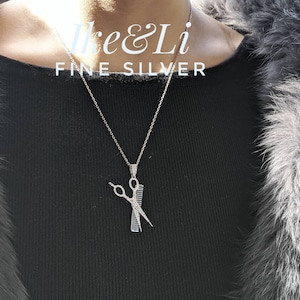 May include: A silver necklace with a pendant shaped like scissors and a comb, encrusted with small, sparkling stones. The necklace is on a silver chain. The image includes the text "Ike & Li FINE SILVER".