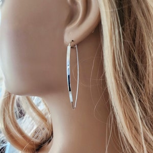 May include: Silver hoop earrings with a thin, flat, and slightly curved design. The earrings are shown on a mannequin's ear.