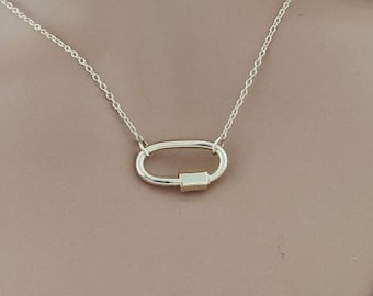 May include: A gold chain necklace with a gold oval-shaped pendant. The pendant is a simple, minimalist design.