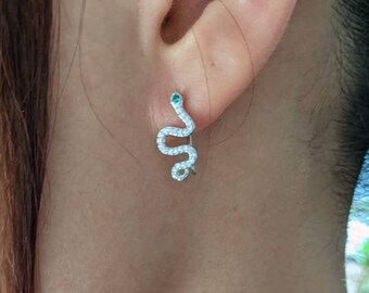 May include: Silver snake earrings with green gemstones. The snake is coiled and has a detailed design.