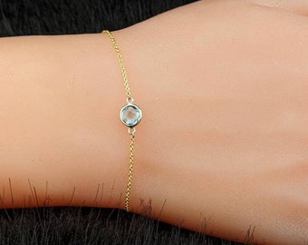 May include: A delicate gold chain bracelet with a single light blue gemstone.