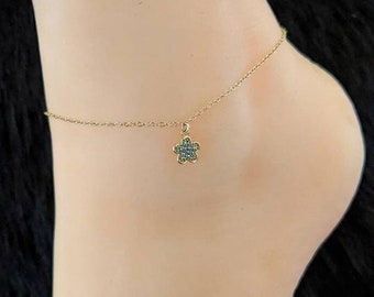 May include: A gold anklet with a small flower charm. The flower is set with clear stones.