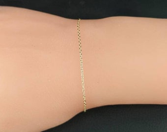 May include: A delicate gold chain bracelet, shown on a model's wrist.