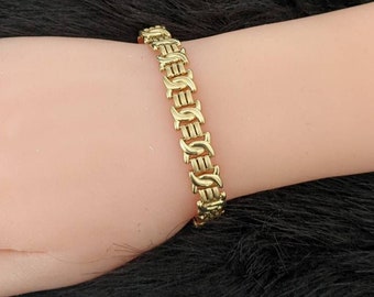 May include: A gold chain bracelet with a unique interlocking design. The bracelet is made of a thick, durable metal and has a polished finish.