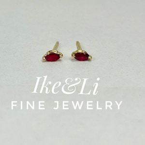 May include: A pair of gold earrings with small, red, marquise-shaped gemstones.