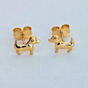 May include: A pair of gold-toned stud earrings featuring a small, detailed dachshund design.
