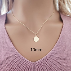 Puede incluir: Un collar de color dorado con un peque&ntilde;o colgante redondo y plano suspendido de una cadena fina. El colgante es circular y liso, con el texto 10mm. claramente visible en negro junto a la pieza de joyer&iacute;a, indicando su tama&ntilde;o exacto.