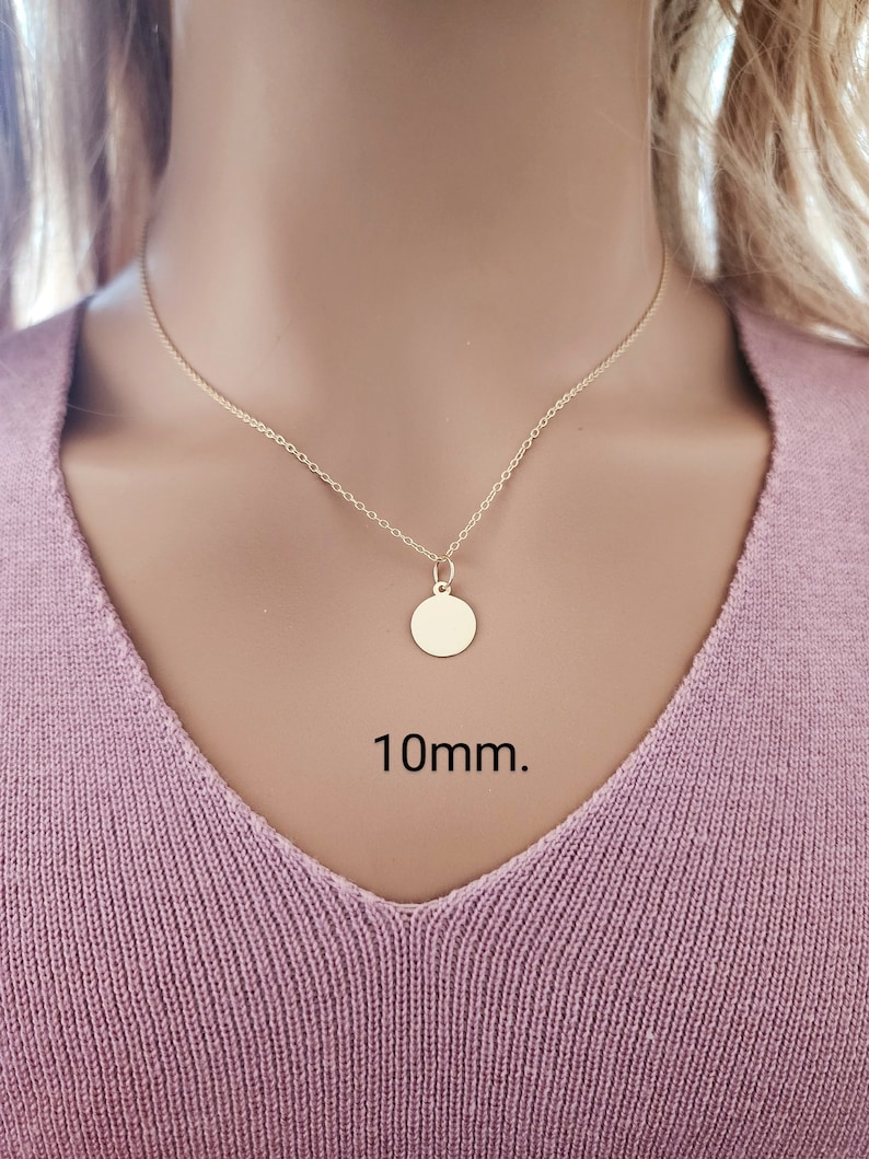 Puede incluir: Un collar de color dorado con un peque&ntilde;o colgante redondo y plano suspendido de una cadena fina. El colgante es circular y liso, con el texto 10mm. claramente visible en negro junto a la pieza de joyer&iacute;a, indicando su tama&ntilde;o exacto.