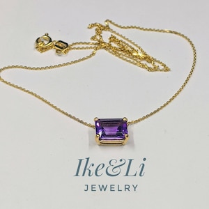 May include: A gold necklace with a rectangular, deep purple gemstone pendant. The chain and pendant setting are gold. The necklace is displayed on a white surface. The text "Ike & Li JEWELRY" is visible below the necklace.