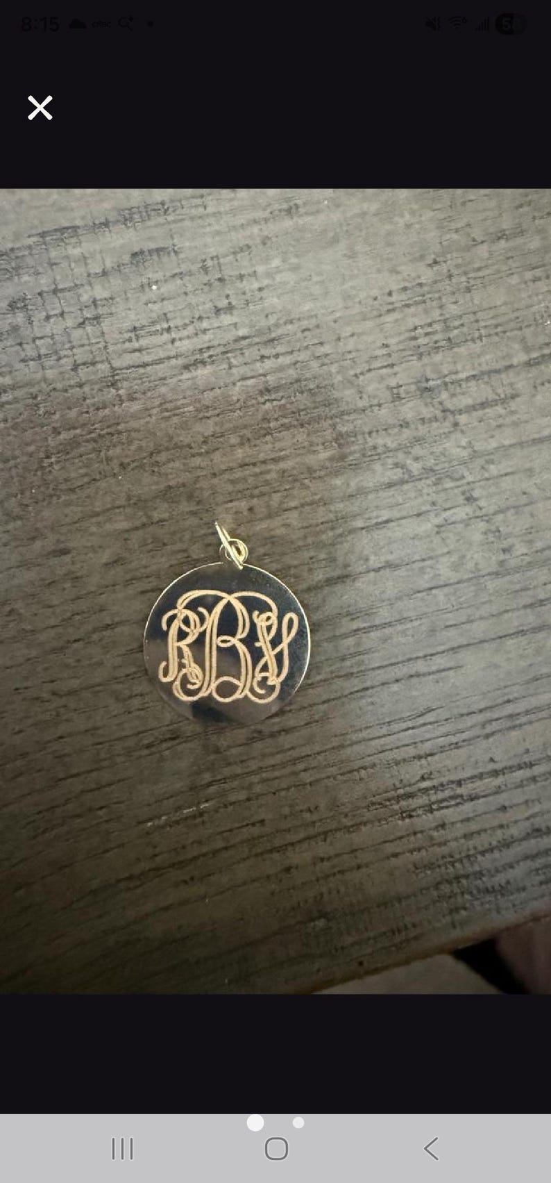 Puede incluir: Un colgante circular de tono dorado que presenta un monograma grabado intrincado con las letras R, B y S entrelazadas en un estilo de escritura decorativo. El colgante incluye una peque&ntilde;a anilla de metal en la parte superior.