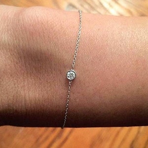 May include: A delicate silver chain bracelet with a single, small, round diamond.