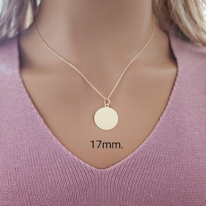 Puede incluir: Un collar de tono dorado que presenta un colgante circular sencillo suspendido de una cadena delicada. El colgante redondo tiene una superficie lisa y pulida, y est&aacute; claramente etiquetado con la medida de 17mm, indicando su tama&ntilde;o.