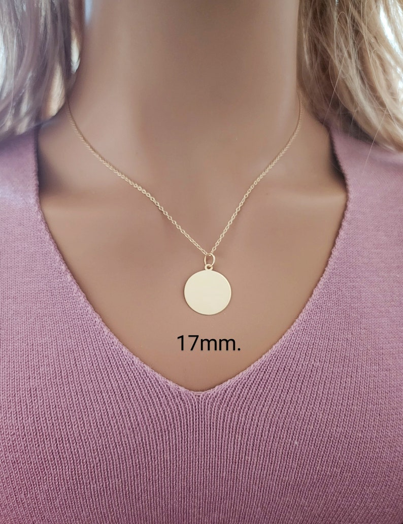 Puede incluir: Un collar de tono dorado que presenta un colgante circular sencillo suspendido de una cadena delicada. El colgante redondo tiene una superficie lisa y pulida, y est&aacute; claramente etiquetado con la medida de 17mm, indicando su tama&ntilde;o.