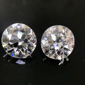 May include: Two clear round diamonds with a faceted cut, set against a black background.