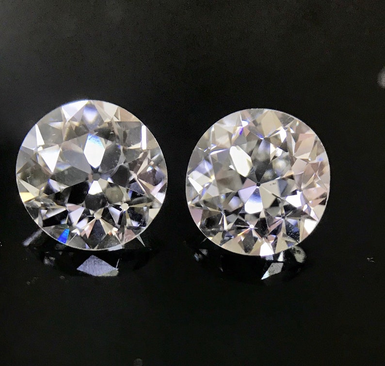 May include: Two clear round diamonds with a faceted cut, set against a black background.