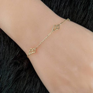 May include: A gold chain bracelet with two delicate heart charms. The hearts are open and interlocked.