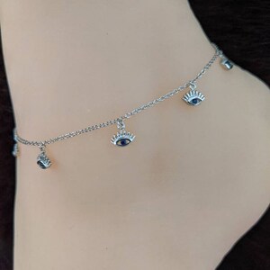 May include: Silver anklet with multiple blue evil eye charms. The anklet is on a mannequin's ankle.