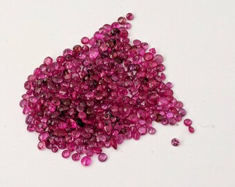 May include: A large pile of small, round, pink gemstones. The gemstones are scattered on a white surface.