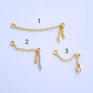 May include: Three gold chain extenders with different styles. The first extender has two loops and a dangling chain. The second extender has two loops and a dangling chain with a smaller chain attached. The third extender has two loops and a dangling chain with a small clear stone at the end.