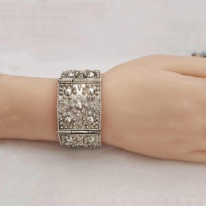 May include: A silver bracelet with a textured, geometric design. The bracelet is made of multiple connected squares with raised circles and lines.