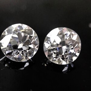 May include: Two clear, round, faceted gemstones on a black background.