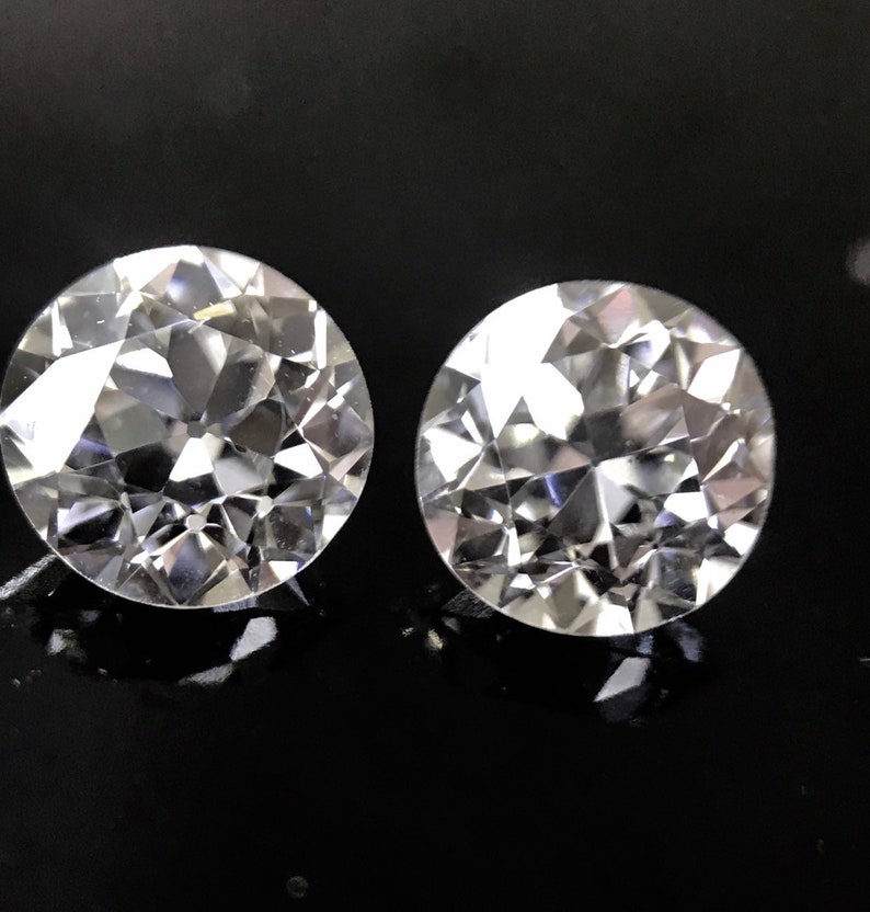 May include: Two clear, round, faceted gemstones on a black background.