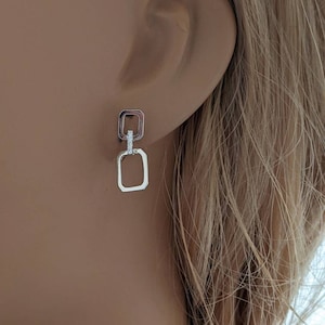 May include: Silver-toned drop earrings featuring a double square design. The top square is connected to the bottom square. The top square has a small row of clear stones. The earrings are shown on a person's ear.