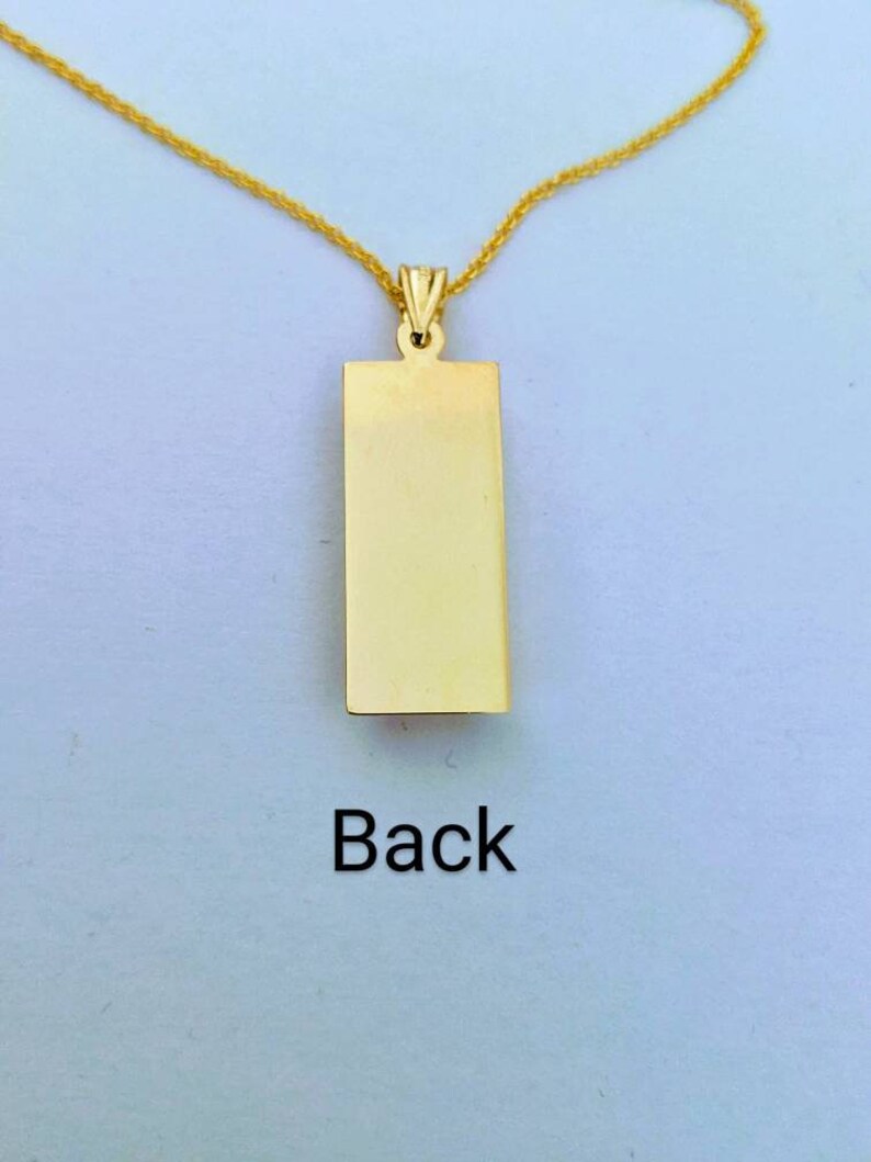 Op de afbeelding: Een goudkleurige rechthoekige hangerketting met bijpassende ketting. De hanger heeft een glad, leeg oppervlak met het woord "Back" in het zwart gedrukt. De ketting wordt gepresenteerd tegen een lichte achtergrond.