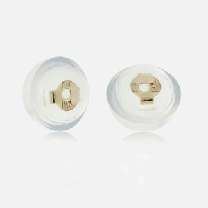 May include: Two clear silicone earring backs, each featuring a small, gold-colored metal clutch insert. The metal inserts are stamped with the text 14K, indicating the material composition of the gold components used in these earring fasteners.