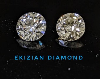 May include: Two round, clear diamonds on a black background. The diamonds are set in a simple, classic style. The text "EKIZIAN DIAMOND" is printed below the diamonds.
