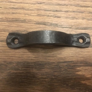 May include: Black metal drawer pull with a rounded top and two holes on either side.