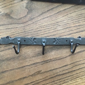 May include: Black metal coat rack with three hooks. The rack is shaped like a dragon with a textured design.