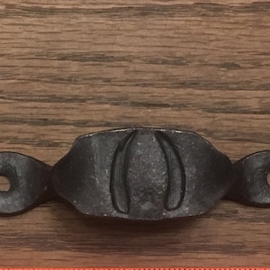 May include: Black metal drawer pull with two holes and a decorative design.